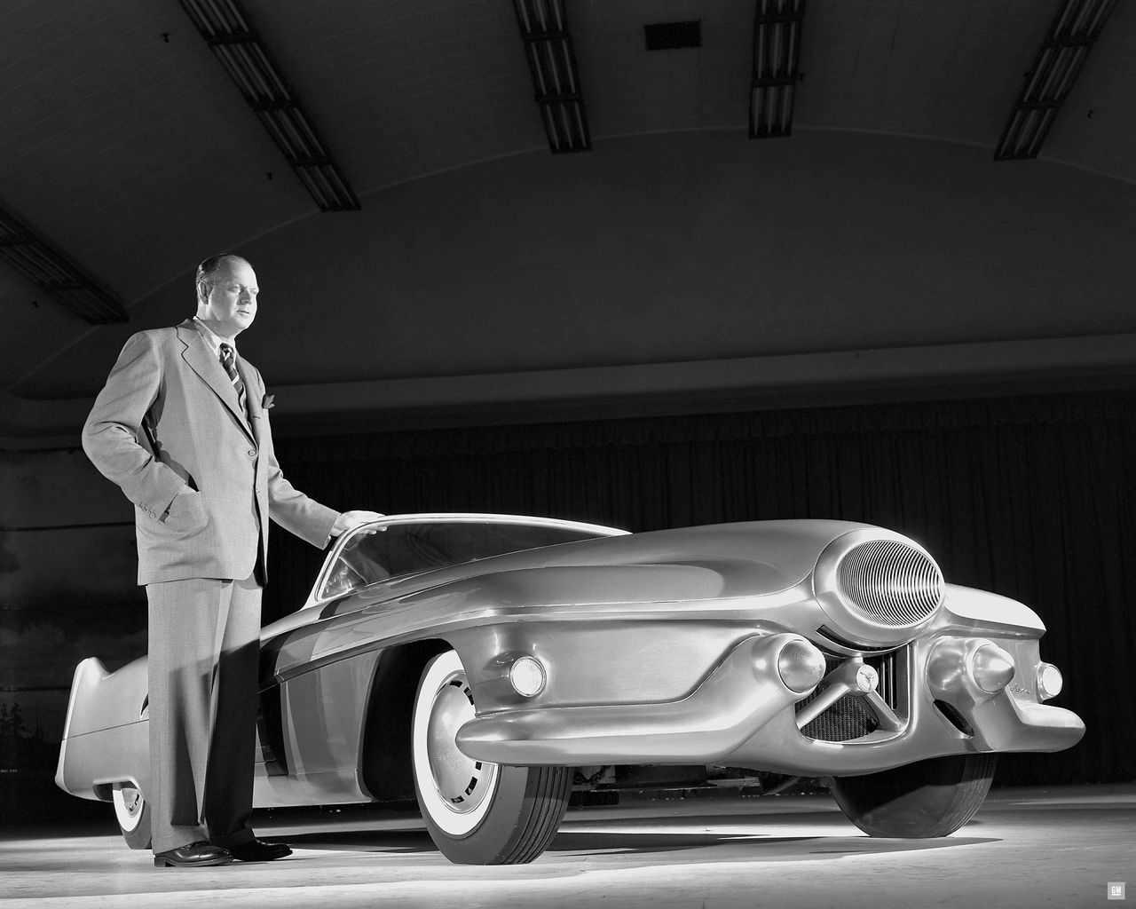 Harley Earl and the Jet Age, captured in one frame. Standing beside his Buick Le Sabre dream car, GM’s styling chief shows the theatrical vision that powered Motorama—and set the stage for Corvette. The Le Sabre’s wraparound glass, fighter-inspired nose, and low, flowing body were less a prototype than a manifesto, proving that an American sports car could be as futuristic as it was beautiful. From spectacles like this, the Corvette’s world was born. (Image courtesy of GM Media LLC.)