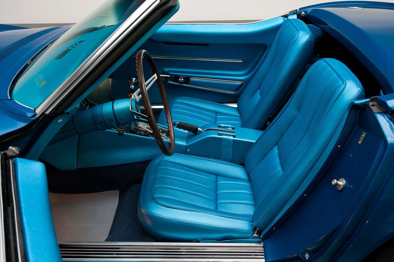 The 1968 Corvette cabin debuted an all-new cockpit that matched the shark body’s drama with a driver-centric layout. Deep round pods carry the speedometer and tach ahead of the wheel, while a bank of auxiliary gauges crowns the center stack—oil pressure, water temp, fuel, volts, and a clock—all angled toward the driver. Lower roof height pushed the fixed-back buckets to a more reclined 33° and ushered in a redesigned console with a proper floor-mounted parking brake and short-throw shifter. Vent wings disappeared as Astro Ventilation introduced cowl-to-rear-deck airflow, and many cars featured the slick fiber-optic lamp monitor on the console—a futuristic nod to system checks. Safety updates—collapsible steering column and standard shoulder belts on coupes—rounded out an interior that felt both racier and more modern than the C2 it replaced. (Image courtesy of RK Motors)