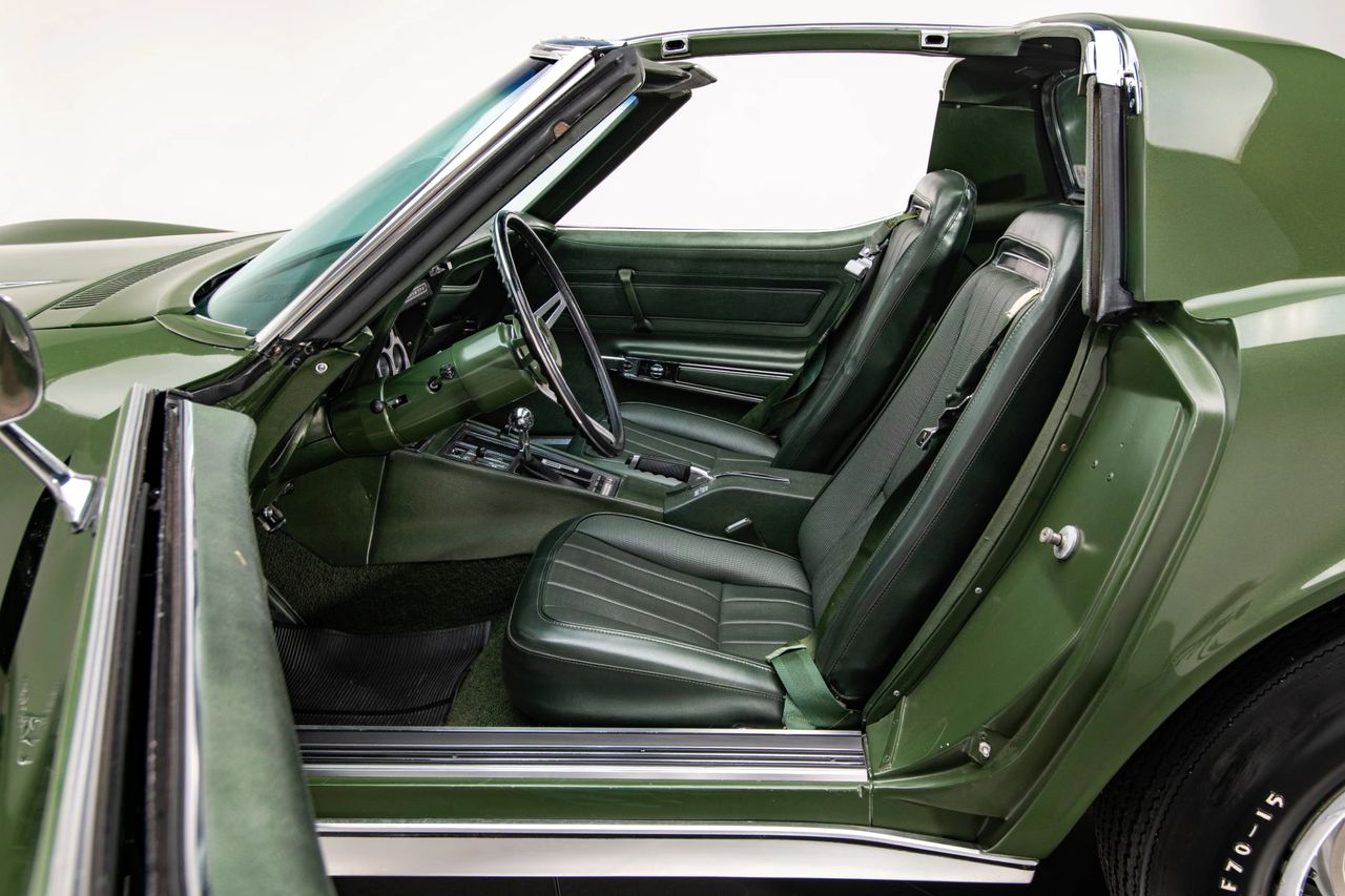 Removable roof panels—and a pop-out rear window—gave the 1970 Corvette coupe near-convertible openness without sacrificing the coupe’s rigidity. Inside, newly introduced high-back buckets with integrated head restraints sat taller and offered better support and safety than earlier low-backs. Chevrolet also cleaned up the cockpit for ’70: the console lost the fussy fiber-optic lamp monitors, leaving a tidier gauge stack around the shifter, while improved belt routing and useful door pockets made the cabin easier to live with. Optioned with the Custom Interior, color-keyed leather and wood-grain trim elevated the otherwise purposeful space.