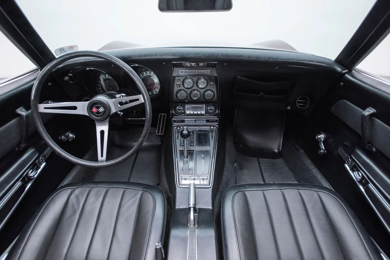 The 1969 Corvette cockpit blends function, focus, and flair in equal measure. Deep-set gauges, toggle switches, and a center stack angled toward the driver emphasize purpose, while high-back bucket seats and a three-spoke steering wheel reinforce the car’s sporting intent. Safety updates like headrests and an energy-absorbing steering column reflect new federal mandates, but nothing dulls the immersive, low-slung driving position. It’s a space that still feels like you wear the car—not just sit in it.
