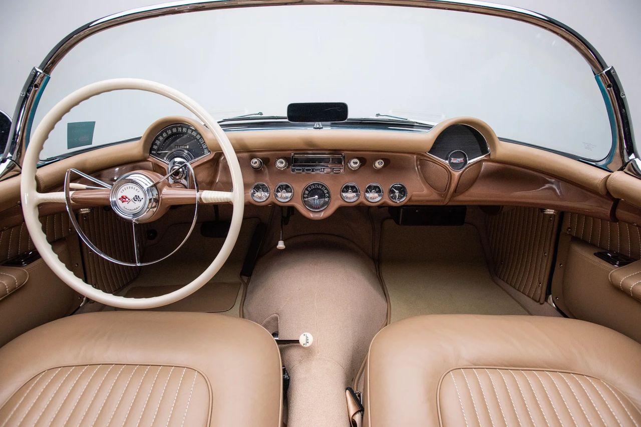 The 1954 Corvette’s interior reflected Chevrolet’s attempt to balance show-car flair with everyday usability. The cockpit featured a full array of aircraft-inspired gauges clustered ahead of the driver, including a large, semi-circular speedometer and six auxiliary dials that gave the dashboard a purposeful look. Chrome-ringed knobs and pushbuttons echoed contemporary appliance design, underscoring the car’s modernist appeal. The bucket-style seats, stitched with vertical pleats, sat low in the fiberglass tub and provided a surprisingly intimate feel for a wide American roadster. Though trim choices were limited—red was paired with most exterior colors while Pennant Blue received beige—the execution was upscale for Chevrolet, setting Corvette apart from the brand’s sedans. More than just a place to sit, the ’54 cockpit was a statement: sporty, focused, and unlike anything else in GM’s stable. (Image courtesy of RK Motors)