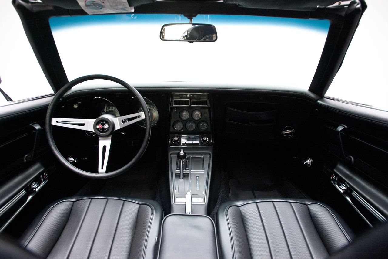 Inside, the 1972 Corvette’s cockpit carried over the familiar C3 “aircraft” layout, but with a noticeably cleaner center console. The biggest change was the deletion of the fiber-optic lamp-monitoring panel, which simplified the console face and gave the gauge/radio stack a less cluttered, more modern look. Minor trim and labeling revisions further freshened the appearance, yet the basic environment—deeply hooded instruments, a tall console running between the seats, and that thin three-spoke wheel—still wrapped the driver in a focused, almost fighter-jet-like driving position. (Image courtesy of RK Motors)