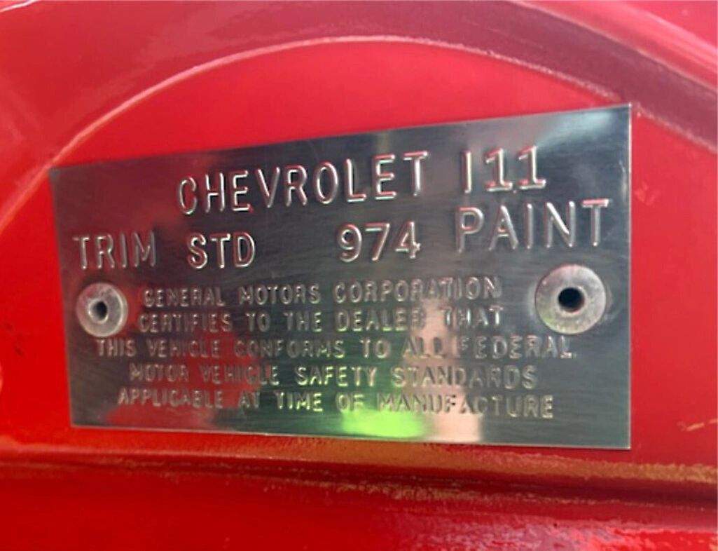 This is the 1968 Corvette trim/paint certification plate, riveted to the driver-side hinge pillar. It shows TRIM: STD (standard vinyl interior) and PAINT: 974, which corresponds to Rally Red for 1968. The tag certifies the car met federal safety standards at the time of manufacture and provides factory-original color/trim data for restorers. Matching this plate to the chassis/VIN and build date is a key step in verifying authenticity.
