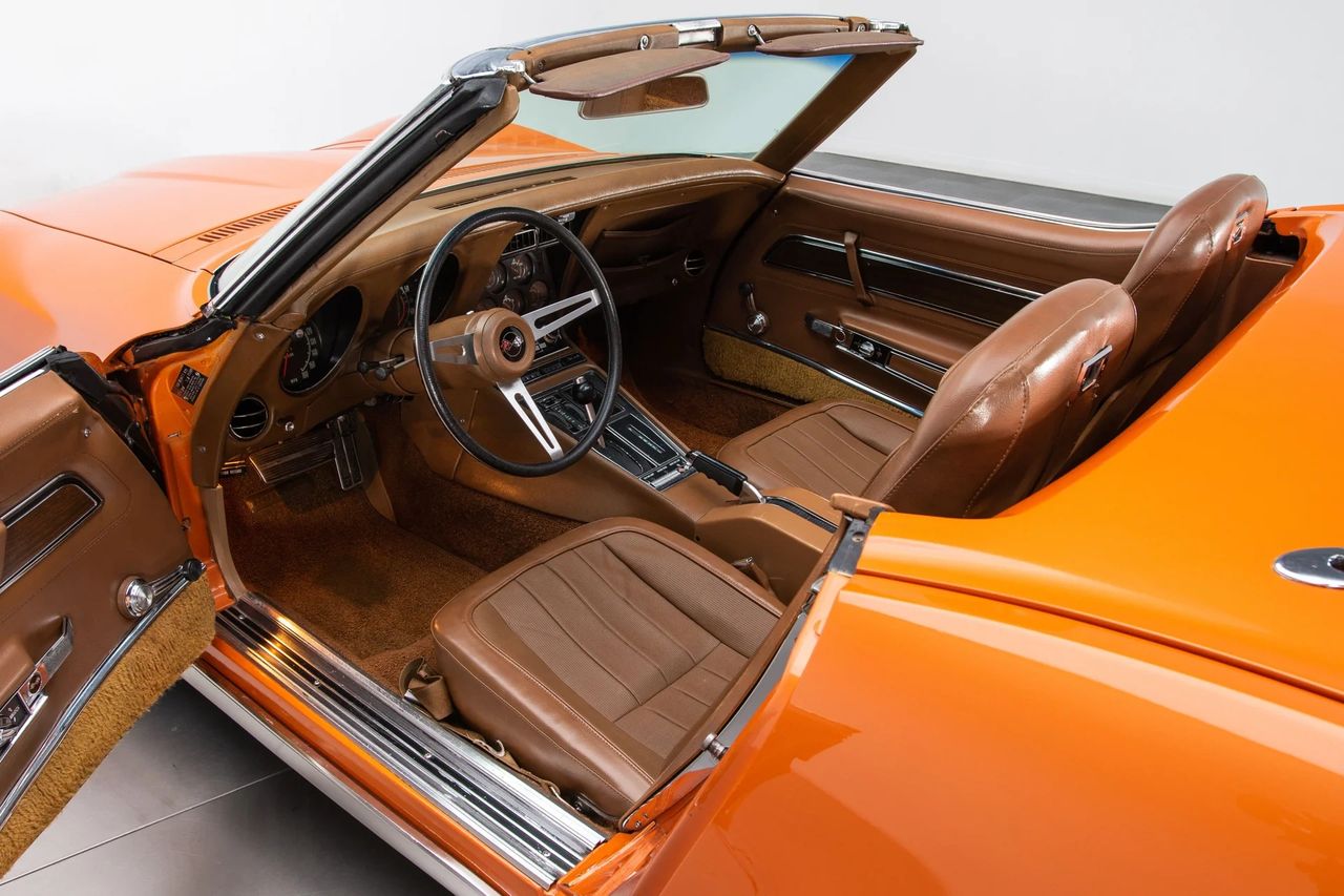 The 1971 Corvette’s interior featured several subtle but meaningful upgrades, many of which are visible in your image. Chevrolet introduced plusher cut-pile carpeting that replaced the coarser loop carpet of earlier years, giving the cabin a warmer, more premium feel. The Saddle vinyl you see here was part of a refreshed color palette for ’71, pairing beautifully with bright trim accents, revised wood-tone appliqués on the console, and the high-back bucket seats that defined early C3 comfort. Combined with the new insulation and improved sound-deadening added for 1971, the cabin delivered a noticeably quieter, more refined driving experience without losing its trademark Stingray attitude. (Image courtesy of RK Motors)