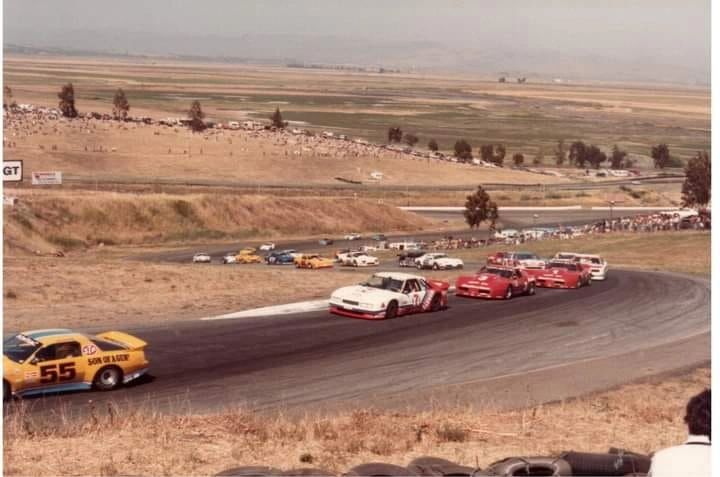 Generational crossroads, frozen on film: Sears Point, 1984—Tom Gloy’s Mercury Capri leads while the brand-new DeAtley C4 Corvette stalks from second. You can feel “racing as it used to be” in the open hillsides, hand-painted numbers, and cars that were loud, imperfect, and gloriously fast. The Capri represents the waning tube-frame era; the Corvette, the production-shape future still finding its feet. It was gritty and human—less corporate, more seat-of-the-pants—and that’s exactly why this series tugs so hard at the memory.