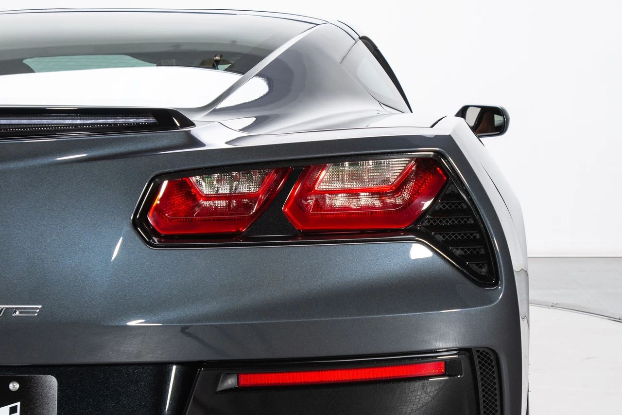 The C7’s faceted taillamps mark a clean break from Corvette’s round-lens tradition—dual LED elements with crisp light pipes framed in a deep, black-chrome bezel. Outboard, the functional aero extractor relieves pressure from the rear fascia, a reminder that every crease earned its place. Above it all, the spoiler packages a slim LED CHMSL, keeping the “third brake light” high and clean in the airstream. Sharp, technical, and purposeful—this is the Stingray’s new rear signature. (Image courtesy of RK Motors)