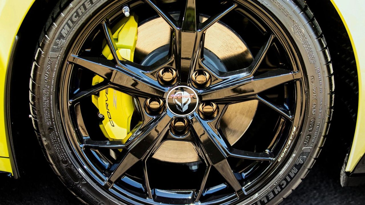 This close-up highlights the Black “Trident” design wheel used on the 2022 Corvette Stingray IMSA GTLM Championship Edition, finished in a deep gloss black to match the car’s race-inspired exterior accents. At the center is the “Jake” logo center cap, one of the quickest visual tells that you’re looking at the Championship Edition-specific wheel package rather than a standard Stingray fitment. Behind it, the yellow Corvette-branded Brembo brake caliper pops through the spokes, reinforcing the edition’s No. 3/No. 4 C8.R-inspired color theme. The Michelin performance tire and large brake rotor filling the barrel complete the picture—this isn’t just an appearance wheel; it’s part of a spec built on the Z51-equipped Stingray foundation. (Image courtesy of GM Media LLC)