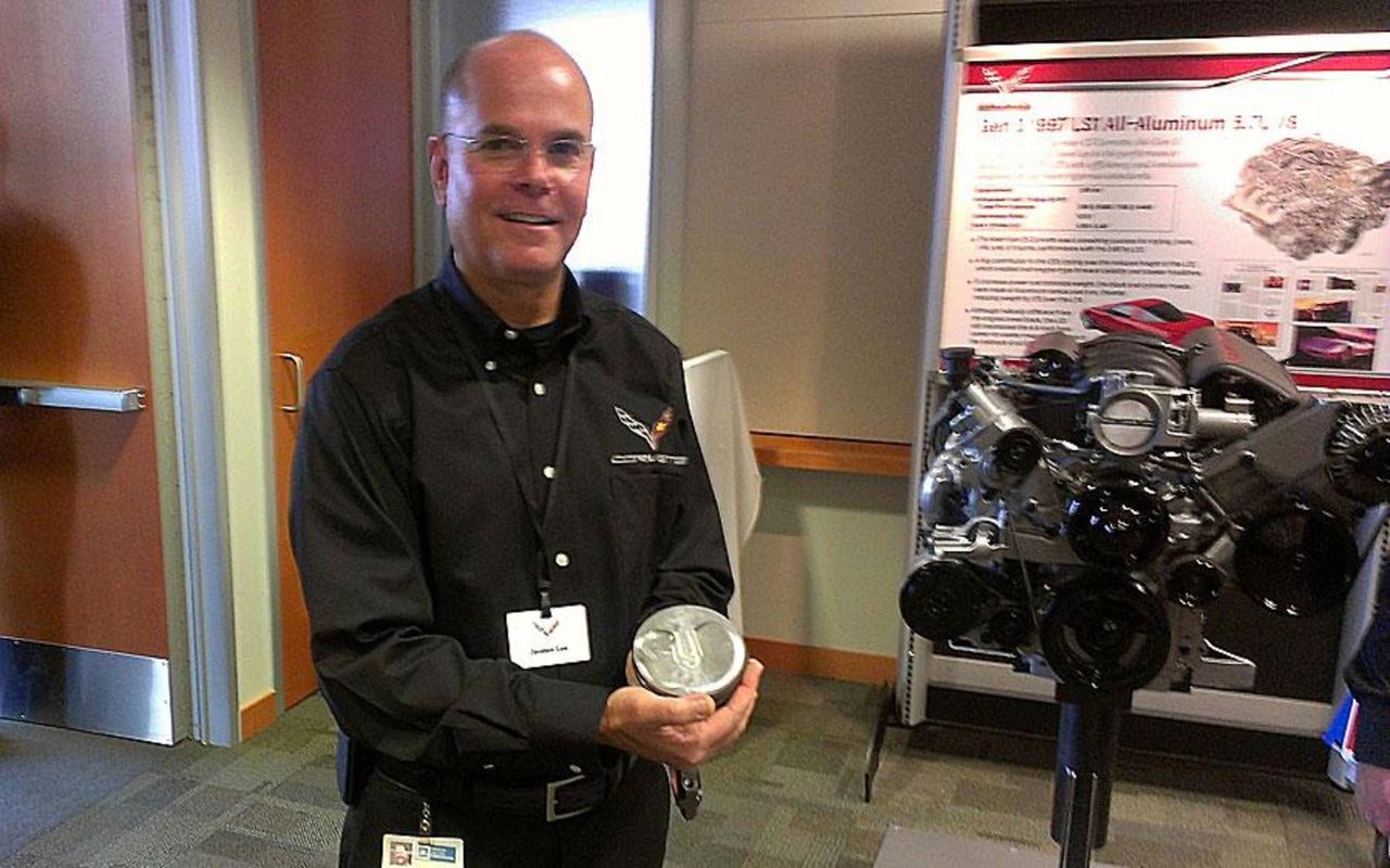 Small-Block Chief Engineer Jordan Lee, shown holding an LT1 piston, was the architect of the Gen-V small-block that powered the 2014 Stingray. He led the move to direct injection, continuously variable valve timing, and AFM—with a sculpted piston bowl and 11.5:1 compression—to deliver broader torque, higher efficiency, and SAE ratings up to 460 hp/465 lb-ft with NPP. Lee’s program set the baseline that made the C7 quicker and thriftier than the C6 while establishing the blueprint for today’s small-block family. (Image courtesy of AutoWeek)