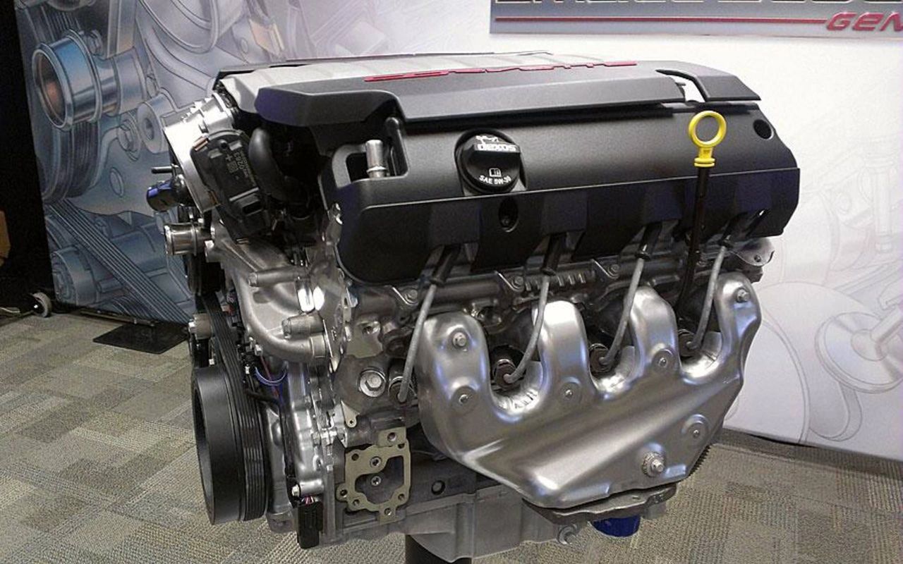 Gen-V LT1 on display: an all-aluminum, deep-skirt block with cross-bolted mains (4.06-in bore/3.62-in stroke, 11.5:1 compression) and coil-near-plug ignition under composite covers for low mass and quiet. Thin-wall stainless exhaust manifolds feed close-coupled catalysts for rapid light-off, while the accessory drive and front cover packaging keep the engine compact in the bay. Base cars used a wet-sump, but Z51 models added a track-ready dry-sump with a remote reservoir to maintain oil pressure under sustained lateral loads.