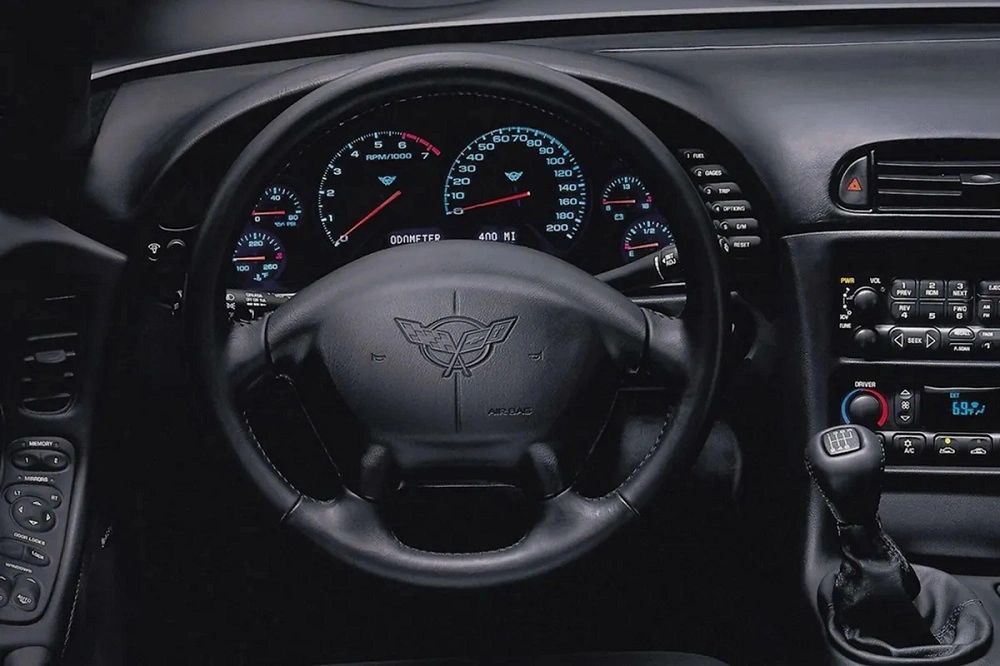 The C5 cabin traded the C4’s digital arcade for crisp analog gauges and a thick, airbag wheel wearing crossed flags. The center stack grouped Bose audio, true climate control, and driver-memory switches within easy reach, while the stubby six-speed shifter fell naturally to hand. Quiet, solid, and functional—this was the first Corvette cockpit that felt genuinely modern.