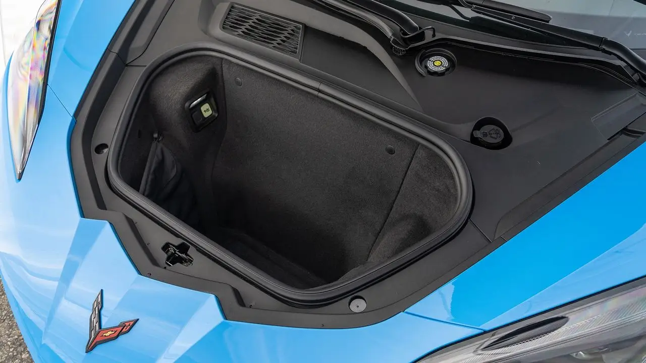 Up front, the C8’s frunk is a deep, squared-off bin that easily swallows a roll-aboard and backpack—perfect when the coupe’s roof panel is riding in the rear. It’s lined and weather-sealed, with power open/close and an interior emergency release, so it’s as everyday-useful as any small hatchback trunk—just in the nose of a mid-engine Corvette. (Image courtesy of Motor Trend)