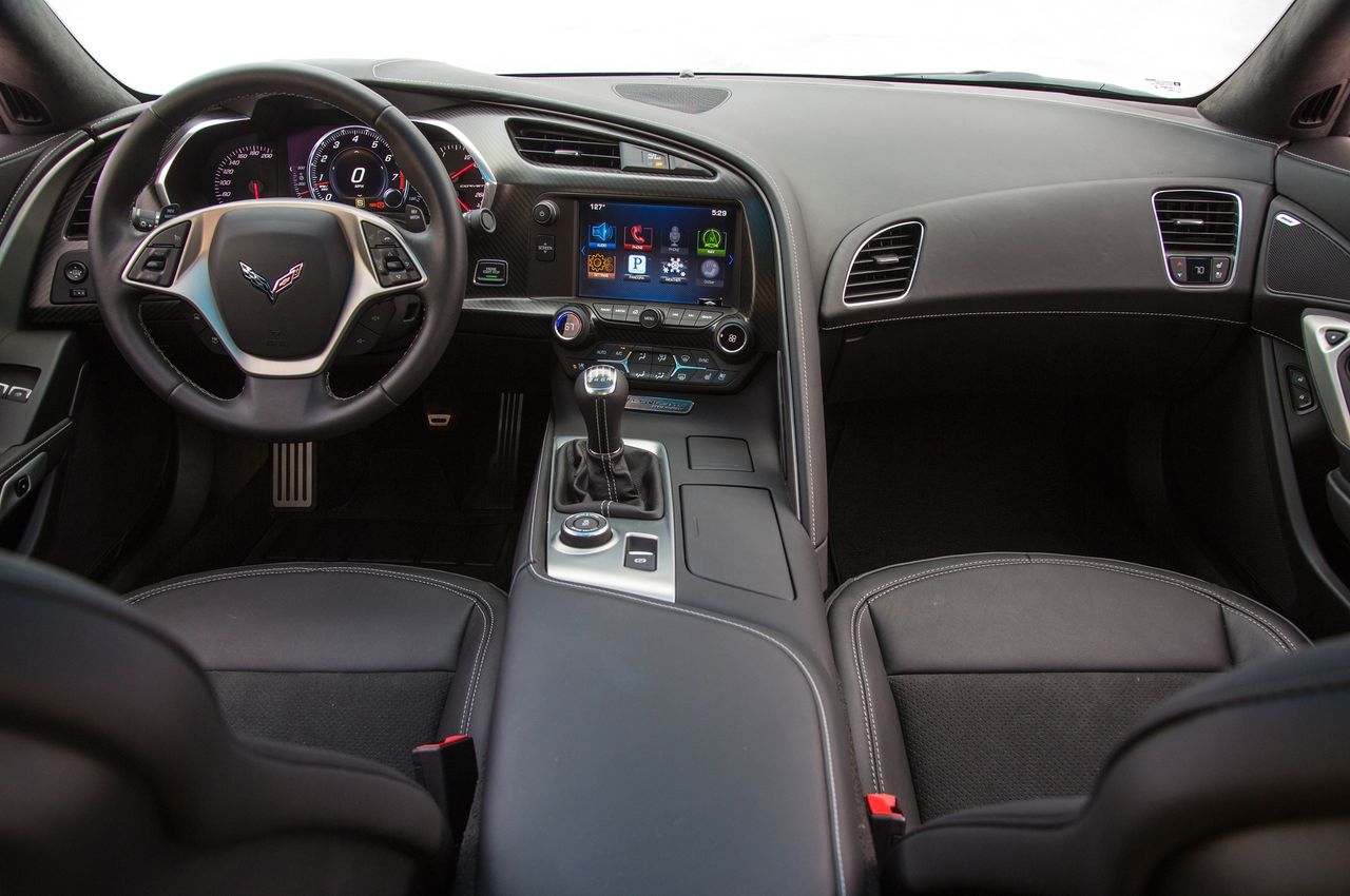 C7 Stingray cockpit: thick-rim wheel, reconfigurable cluster with color HUD, 8-inch MyLink screen (with hidden cubby), and a 7-speed manual beside the drive-mode dial—all set in a fully wrapped, stitched cabin that finally feels premium.