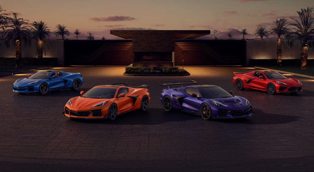 2025 Chevrolet Corvette lineup image showing the C8 Stingray, E-Ray, Z06, and 2025 ZR1 parked together at dusk in front of a modern estate, illustrating the full evolution of the mid-engine Corvette family from entry model to 1,064-horsepower flagship.