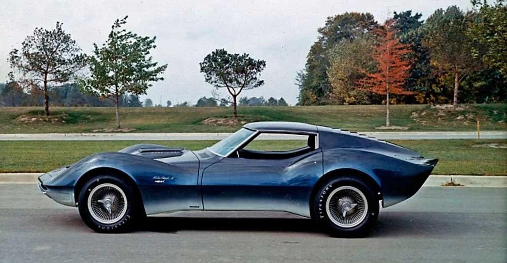 There are more echoes between XP-819 and the Mako Shark II than most people realize. Both cars came out of the same late-’50s/early-’60s GM Styling mindset, with Larry Shinoda and his team pushing a dramatic “Coke-bottle” plan view: narrow in the middle, swelling over the wheelarches, and tapering to sharp points at the nose and tail. The XP-819’s front fenders and the Mako Shark II’s are remarkably similar in the way they rise and then fall toward a low, almost knife-edge front end, and both use a very low, compact greenhouse that visually sits down into the body rather than perched on top of it. The rear quarters share that muscular, hipped look that would later define the C3 Corvette, with a pronounced “waist” ahead of the rear wheels and a long deck stretching rearward. Where the two diverge is largely mechanical—the XP-819 packaging everything around a rear engine and transverse layout, the Mako Shark II previewing a more conventional front-engine C3—but visually you can clearly see them as parallel branches of the same aggressive, surfacing-driven Corvette design language. (Image courtesy of GM Media LLC) There are more echoes between XP-819 and the Mako Shark II than most people realize. Both cars came out of the same late-’50s/early-’60s GM Styling mindset, with Larry Shinoda and his team pushing a dramatic “Coke-bottle” plan view: narrow in the middle, swelling over the wheelarches, and tapering to sharp points at the nose and tail. The XP-819’s front fenders and the Mako Shark II’s are remarkably similar in the way they rise and then fall toward a low, almost knife-edge front end, and both use a very low, compact greenhouse that visually sits down into the body rather than perched on top of it. The rear quarters share that muscular, hipped look that would later define the C3 Corvette, with a pronounced “waist” ahead of the rear wheels and a long deck stretching rearward. Where the two diverge is largely mechanical—the XP-819 packaging everything around a rear engine and transverse layout, the Mako Shark II previewing a more conventional front-engine C3—but visually you can clearly see them as parallel branches of the same aggressive, surfacing-driven Corvette design language. (Image courtesy of GM Media LLC)