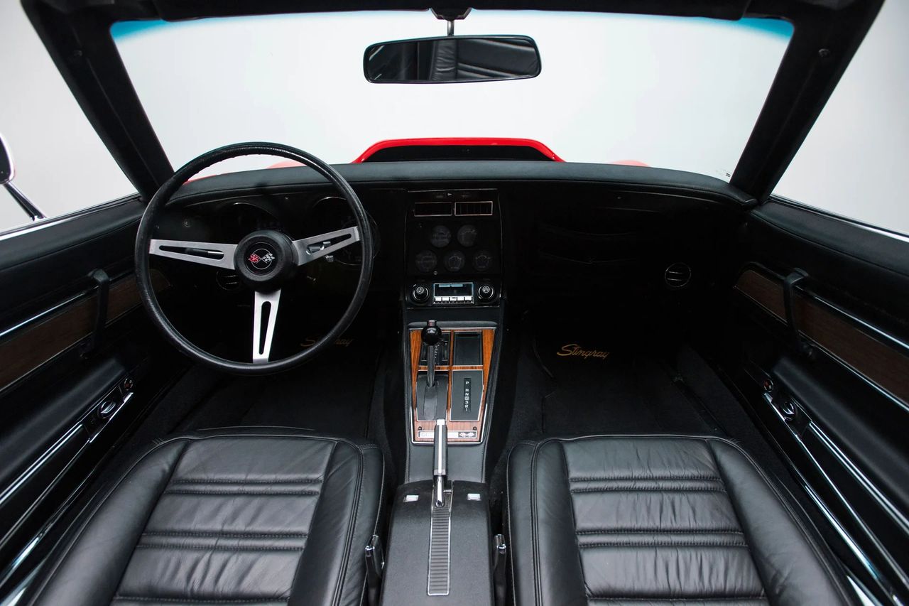 Viewed from the driver’s seat, the 1974 Corvette’s cockpit is pure C3: a driver-centric dash wrapped in textured vinyl, deep-bolstered bucket seats, and a center stack packed with auxiliary gauges framed by faux woodgrain. Chevrolet offered buyers a choice of vinyl or optional leather upholstery that could be paired with an unusually rich set of color options for the era. Beyond traditional black, interiors could be ordered in Dark Blue, Dark Red, Medium Saddle, Neutral, or even Silver—hues that allowed owners to create striking combinations with the year’s exterior palette. Pairings like Classic White over Silver or Bright Yellow over Saddle gave the 1974 Corvette a distinctly upscale, fashion-forward presence, demonstrating how interior materials and colors were used to keep the model feeling premium and modern despite the industry’s tightening regulatory and performance constraints. (Image courtesy of RK Motors)