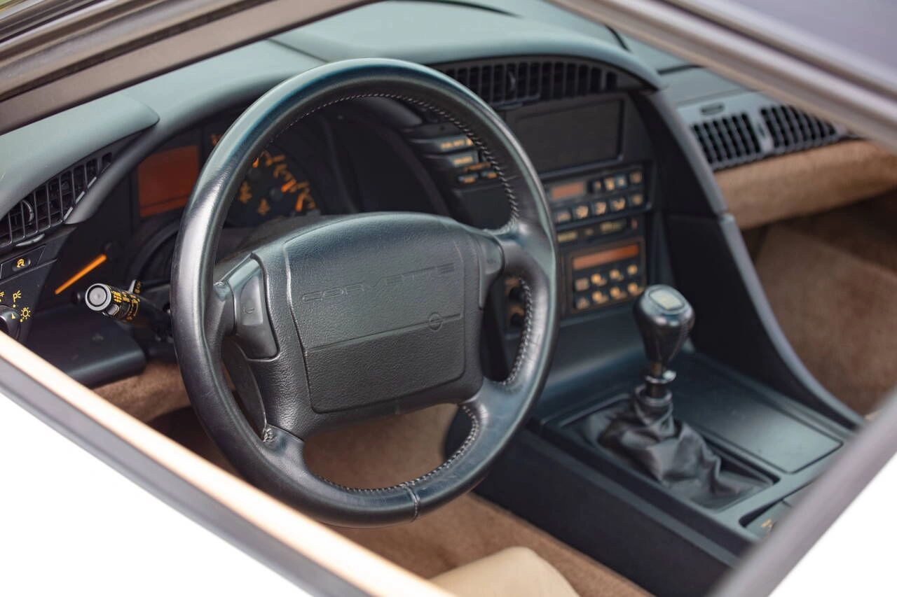 The cockpit of a 1992 Corvette: a driver-focused interior with digital/analog hybrid gauges, the signature squared-off steering wheel embossed with Corvette, and the no-cost-option 6-speed manual shifter—offering enthusiasts the purest connection to the new LT1 small-block under the hood.