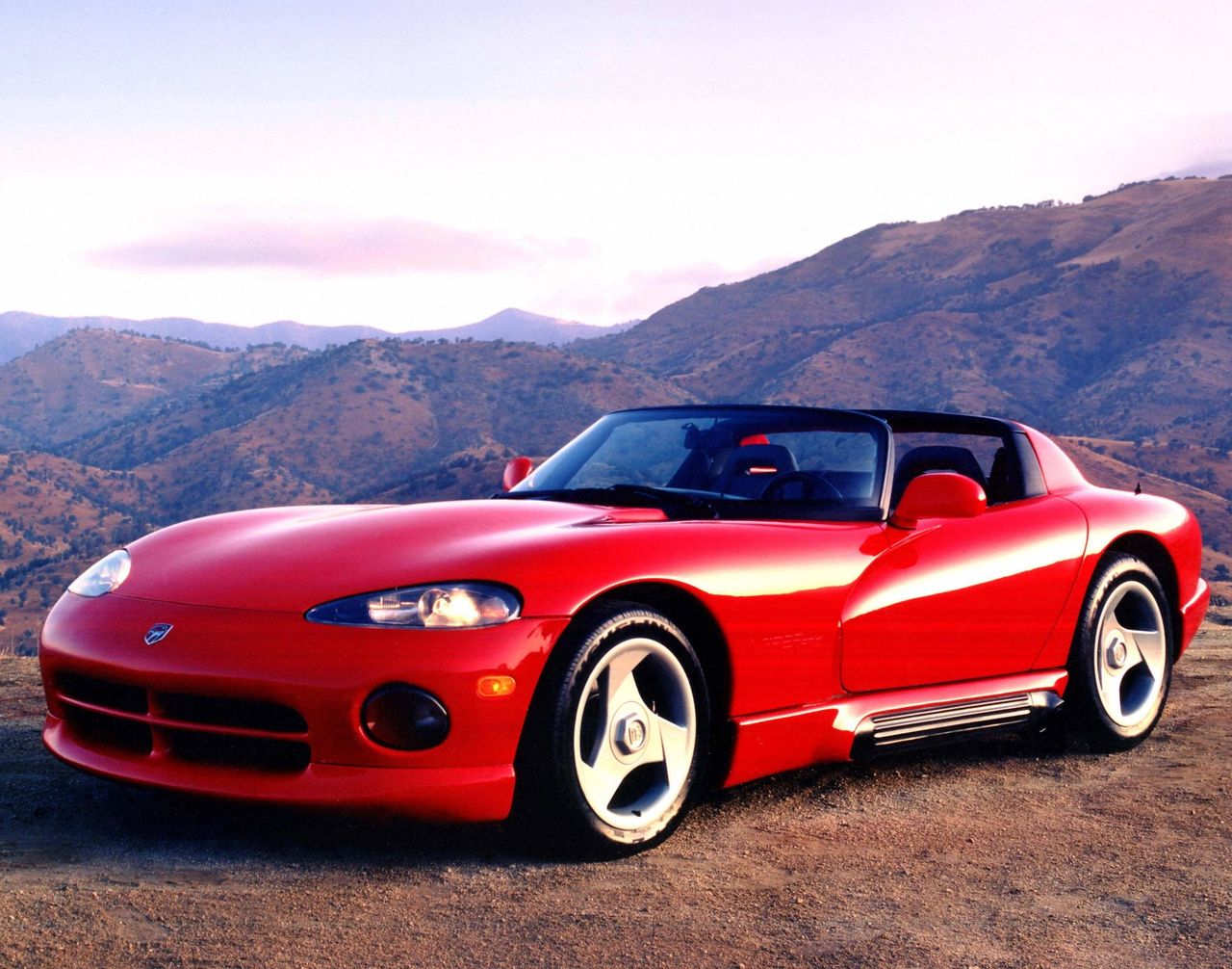 When Dodge unveiled the 1991 Viper RT/10, it fired a direct shot across Corvette’s bow—especially at the reigning “King of the Hill,” the ZR-1. Where the ZR-1 showcased high-tech sophistication with its Lotus-designed LT5 and refined road manners, the Viper was raw and unapologetic: a brutal, V10-powered throwback to the muscle car ethos. With no roof, no side windows, and side pipes that could sear your calf, the Viper embodied pure excess, a brash counterpoint to the Corvette’s precision. Together, they defined two very different visions of American performance in the early ’90s—one polished and world-class, the other wild and untamed.