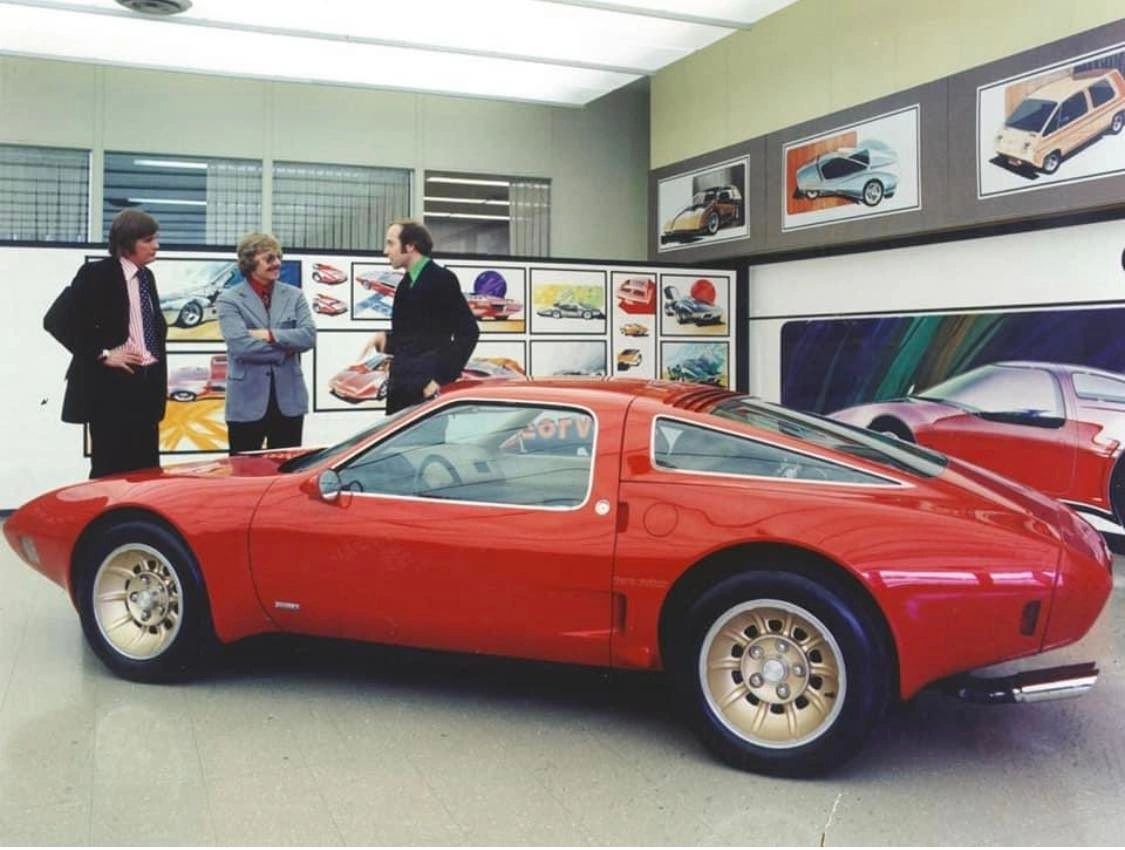 Hank Haga (left), Kip Wasenko (center), and Otto Soeding at the GM Design Center. During XP-987 GT development, some accounts suggest that GM was sensitive to how a Corvette-branded concept built in Italy might be perceived under evolving import and homologation rules in Europe. According to these stories, the car initially returned to Detroit simply as the “Chevrolet GT,” with Corvette identity and “Two-Rotor” graphics added later for press photography and auto-show duty. However, no known GM archival documents definitively confirm that this sequencing was driven by tax or regulatory necessity, so it’s best understood as a widely repeated anecdote rather than settled fact. What is clear is that XP-987 GT had to navigate not just engineering and styling hurdles, but also the corporate and political sensitivities of launching an American halo car with foreign coachwork during an era of oil shocks and trade tensions. (Image courtesy of GM Media LLC) Hank Haga (left), Kip Wasenko (center), and Otto Soeding at the GM Design Center. During XP-987 GT development, some accounts suggest that GM was sensitive to how a Corvette-branded concept built in Italy might be perceived under evolving import and homologation rules in Europe. According to these stories, the car initially returned to Detroit simply as the “Chevrolet GT,” with Corvette identity and “Two-Rotor” graphics added later for press photography and auto-show duty. However, no known GM archival documents definitively confirm that this sequencing was driven by tax or regulatory necessity, so it’s best understood as a widely repeated anecdote rather than settled fact. What is clear is that XP-987 GT had to navigate not just engineering and styling hurdles, but also the corporate and political sensitivities of launching an American halo car with foreign coachwork during an era of oil shocks and trade tensions. (Image courtesy of GM Media LLC)