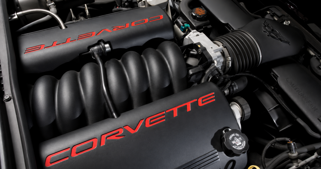 Close-up of the 2001 Chevrolet Corvette LS1 engine bay, showing the black composite intake manifold, red Corvette lettering on the engine covers, throttle body, air intake assembly, and surrounding components in clean, restored condition.