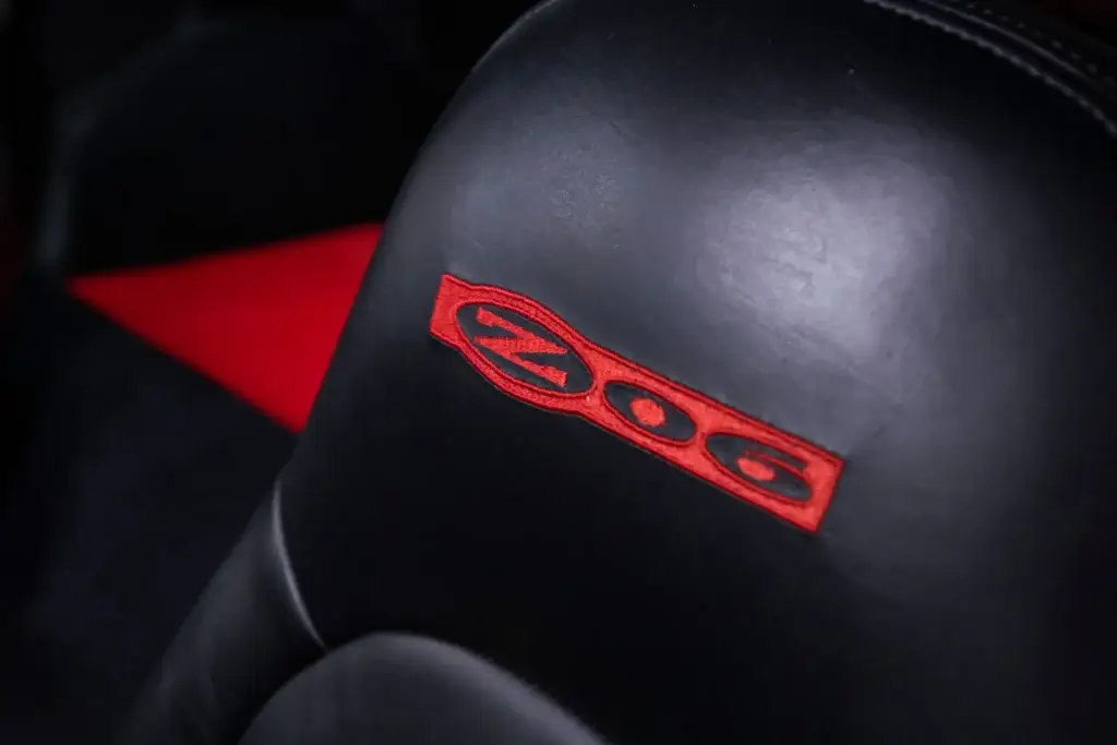 Close-up of a black leather 2001 Chevrolet Corvette Z06 seat headrest featuring a red embroidered Z06 logo, with a red seat insert visible in the background.