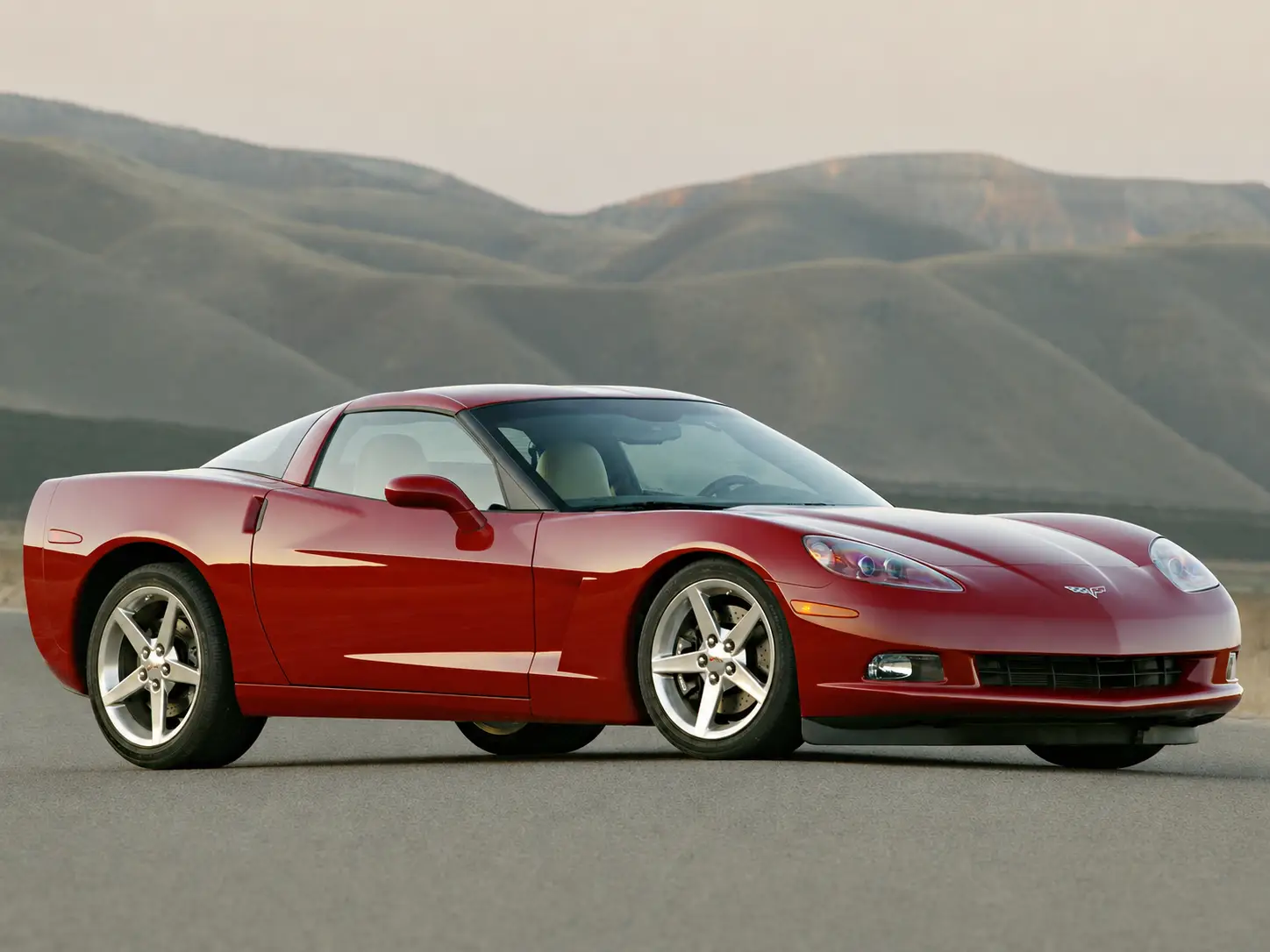 The 2005 red Corvette Coupe is parked in front of a mountain range.
