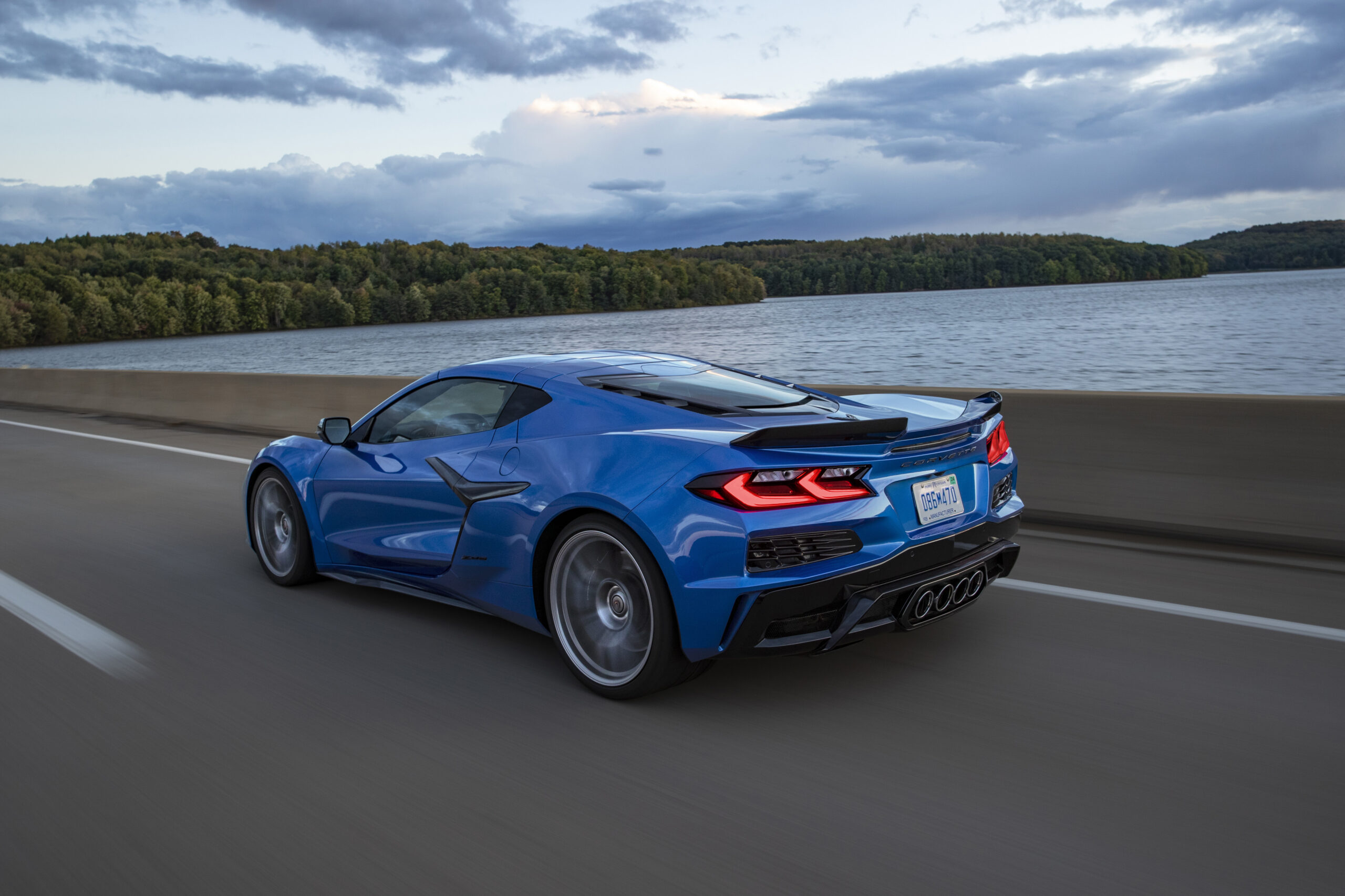 Rear 7/8 view of 2023 Chevrolet Corvette Z06 in Elkhart Lake Blue Metallic driving down a road.