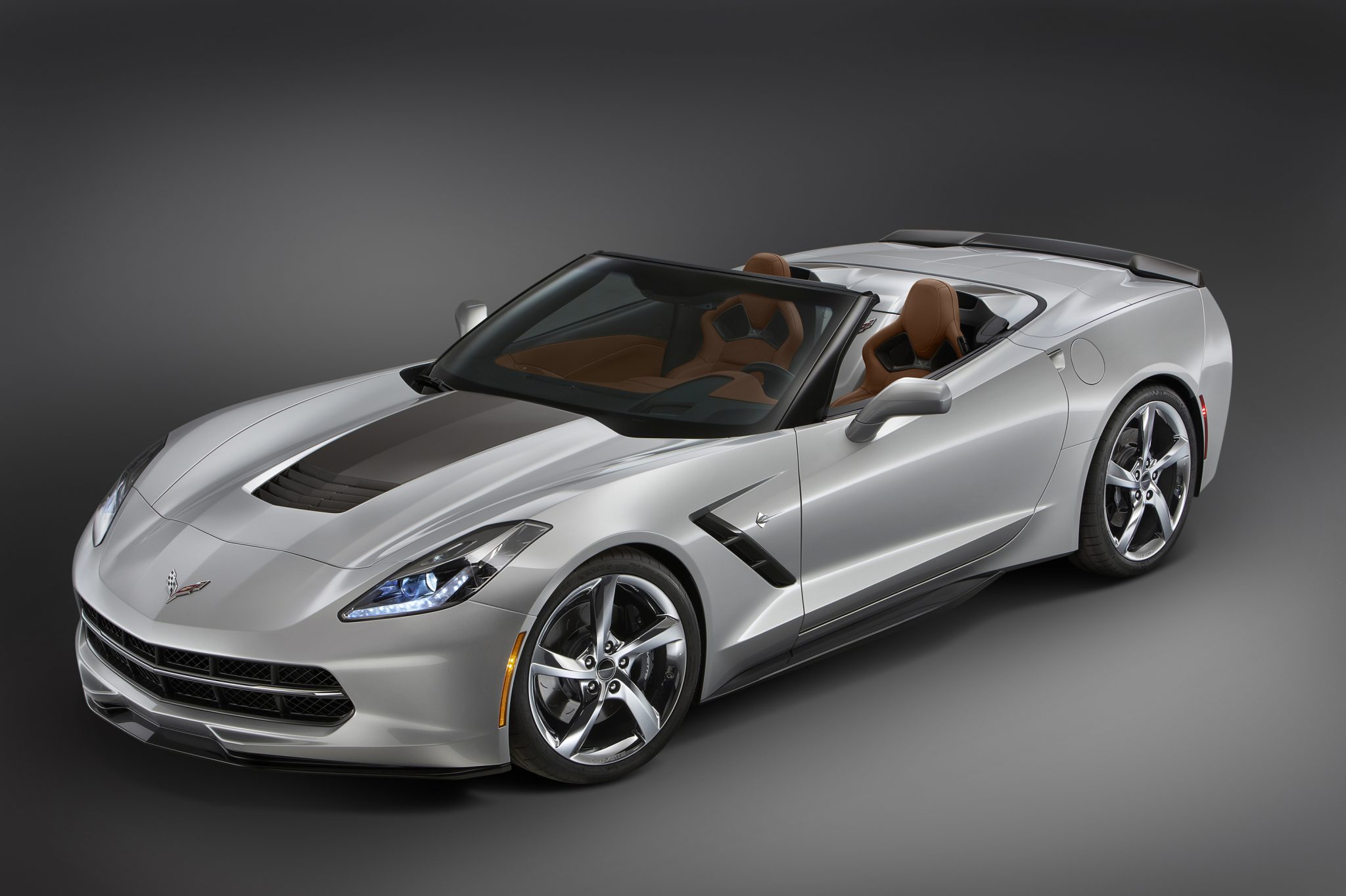 Silver 2015 Chevrolet Corvette Stingray convertible equipped with the Atlantic Design Package, shown in a bright showroom with chrome wheels, Shark Gray exterior accents, a front splitter, and a saddle-tan interior.