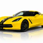 Yellow 2015 Chevrolet Corvette Stingray shown in a front three-quarter view, featuring black racing stripes and black wheels, isolated against a white studio background with a softly fading mirrored reflection beneath the car.
