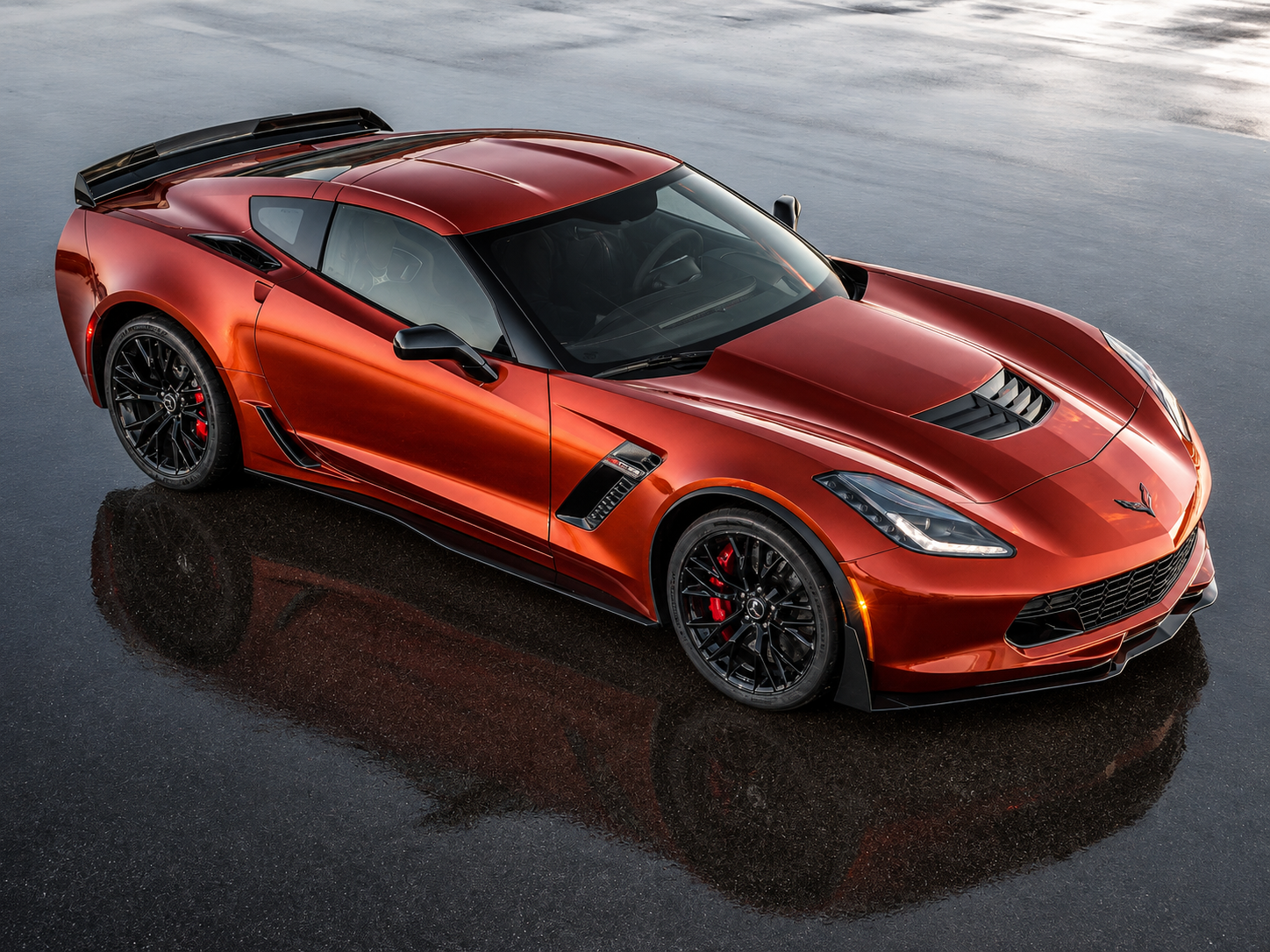 Metallic red 2015 Chevrolet Corvette Z06 shown from an elevated front three-quarter angle, highlighting its widened bodywork, large hood extractor, black wheels, front splitter, functional cooling vents and prominent rear aerodynamic hardware.