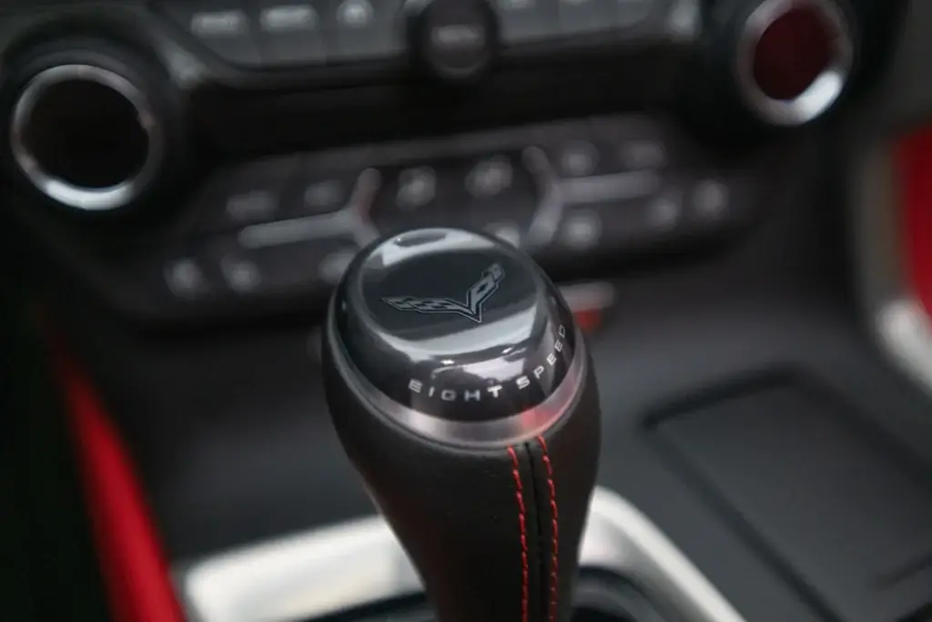 Close-up of the eight-speed automatic transmission shifter in a 2015 Chevrolet Corvette Z06, featuring the crossed-flags emblem, EIGHT SPEED lettering and red contrast stitching.