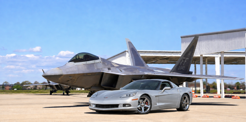 2005 Silver Corvette parked in front of an F-22 Raptor.