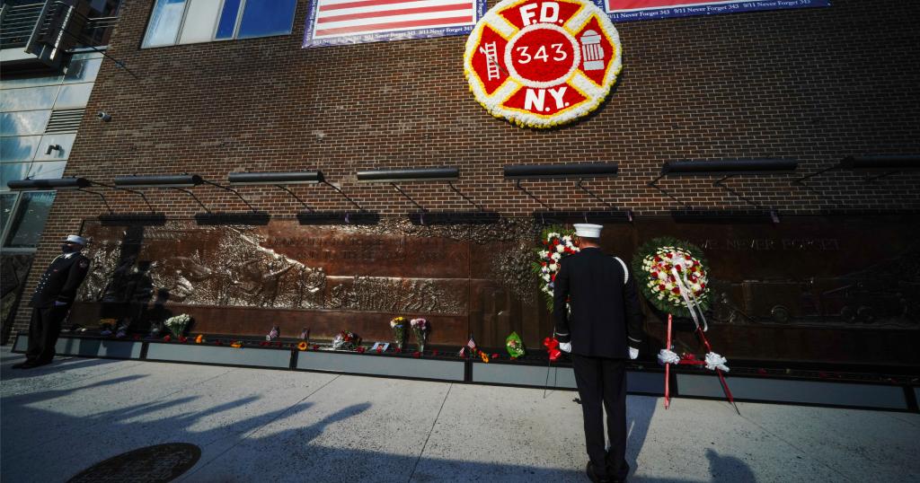 An FDNY firefighter stands in quiet remembrance before the FDNY Memorial Wall, beneath a large 343 emblem honoring the 343 New York City firefighters who died on September 11, 2001.