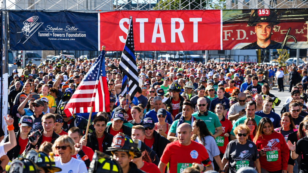 Thousands of participants, including firefighters and first responders, gather beneath the starting banner for the annual Tunnel to Towers 5K Run & Walk honoring FDNY firefighter Stephen Siller and raising money for the foundation established in his memory.