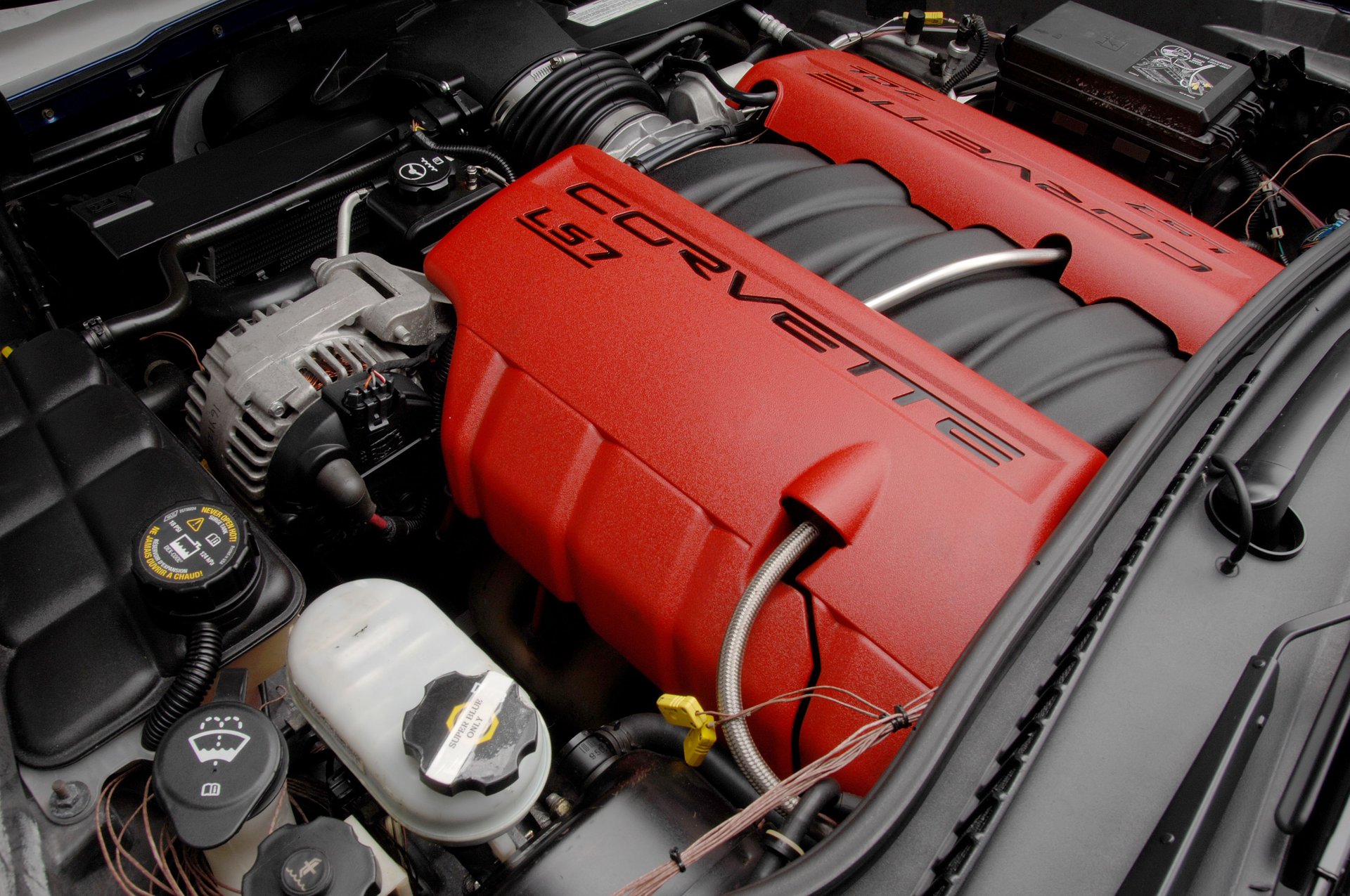 Close-up photograph of the 7.0-liter LS7 V8 engine installed in a 2006 Chevrolet Corvette Z06, featuring distinctive red engine covers with black Corvette and LS7 lettering, a black composite intake manifold, aluminum alternator, air intake ducting, and surrounding engine-bay components.