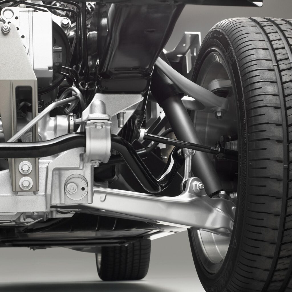 Technical illustration of the sixth-generation Chevrolet Corvette's independent suspension architecture, showing aluminum upper and lower control arms, transverse composite leaf spring, shock absorber, and associated mounting hardware. The illustration demonstrates the fundamental suspension geometry shared by the standard C6 Corvette and the 2006 Z06, which featured model-specific suspension calibration.