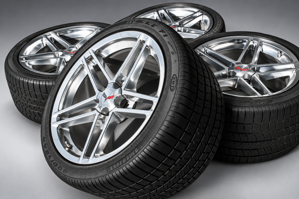 Close-up photograph of polished five-spoke Corvette wheels fitted with wide Goodyear Eagle F1 performance tires, arranged together against a neutral charcoal-gray studio background. The image highlights the wheels' metallic finish, Corvette crossed-flags center caps, low-profile tire sidewalls, and broad tread surfaces, illustrating the high-performance wheel and tire technology associated with the 2006 Corvette Z06.